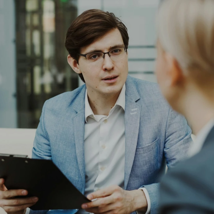 Man in suit holding clipboard talking to woman